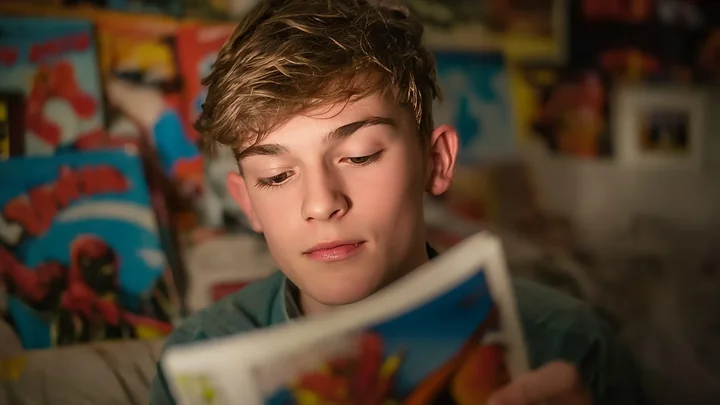 Zdjęcie przedstawia chłopca (nastolatka) czytającego komiks