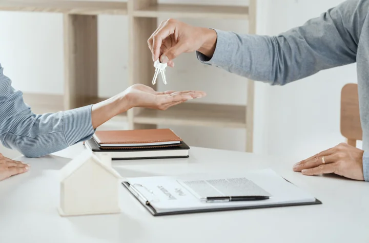 w biurze męska, nad białym biurkiem z dokumentami ręka podaje klucze kobiecie 
