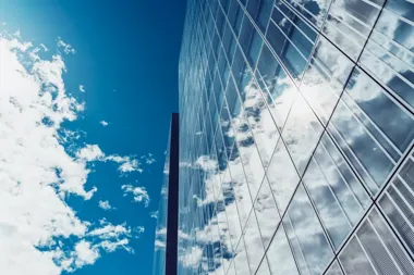 Szklany wieżowiec odbijający chmury na tle błękitnego nieba