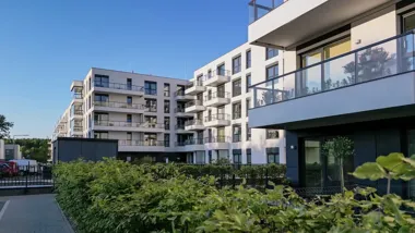 Nowoczesne apartamentowce z balkonami i zielonym żywopłotem pod błękitnym niebem.