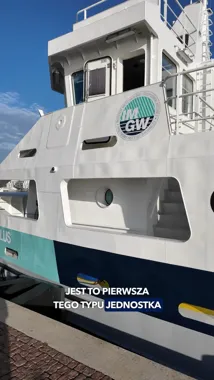 Fragment białej jednostki pływającej z logo IM GW, cumującej przy nabrzeżu w słoneczny dzień.