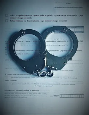 Policyjne kajdanki leżą na wydruku formularza dotyczącego nakazu opuszczenia wspólnie zajmowanego mieszkania.