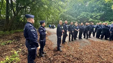 Funkcjonariusze policji w mundurach zgromadzeni na leśnej drodze podczas odprawy służbowej.