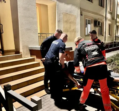 Policjanci i ratownicy medyczni przenoszą osobę na noszach przed budynkiem nocą.