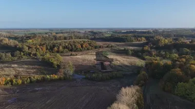 Widok z lotu ptaka na rozległą, częściowo zalesioną i zabudowaną dolinę w okresie jesiennym, z widocznymi polami, lasami oraz niewielkimi zabudowaniami w oddali