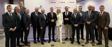 Grupa osób w formalnym stroju pozuje do zdjęcia podczas wydarzenia biznesowego z logo firmy Rënk w tle.