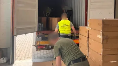 Funkcjonariusze Służby Celno-Skarbowej przeprowadzają kontrolę ładunku kartonów w naczepie ciężarówki.