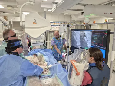 Zespół medyczny w sali operacyjnej wykonuje zabieg kardiologiczny przy użyciu sprzętu do angiografii i monitorowania pacjenta.