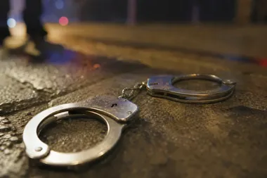Kajdanki leżą na mokrej nawierzchni ulicy nocą, w tle rozmyte światła i sylwetka przechodnia.